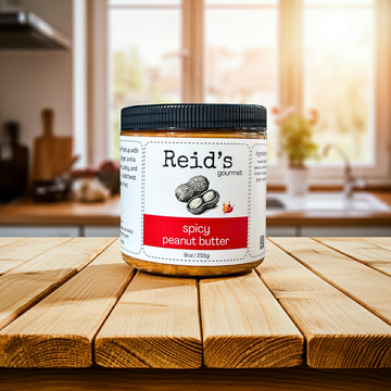 Jar of Reid's Gourmet spicy peanut butter on a wooden table with a kitchen background
