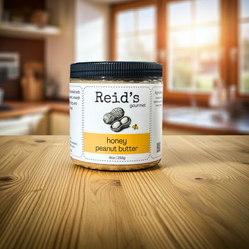Jar of Reid's gourmet honey peanut butter on a wooden table with a kitchen background