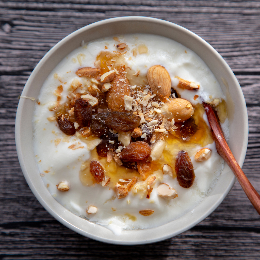 bowl of greek yogurt topped with raisins, nuts, and cinnamon whipped honwy